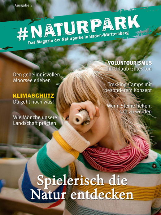 Titelbild des #Naturpark Magazins. Darauf ist ein Kind in einem bunten Wollpullover abgebildet, dass durch einen hohlen Ast in die Kamera schaut. 