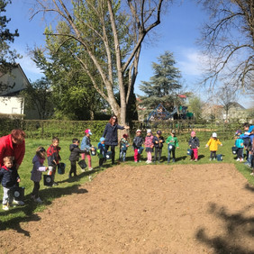 Kinder und Erzieherinnen des Kindergartens Erhardtstraße in Herrenberg säen eine Wildblumenfläche ein. Foto: Rainer Wolf Kinder und Erzieherinnen des Kindergartens Erhardtstraße in Herrenberg stehen um eine gefräste Fläche und werfen Samen