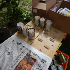 Die Dosen sind fertig gefüllt. Nur noch ein paar Minuten warten, bis das Wachs abgekühlt ist. it Röhrchen gefüllte Dosen stehen auf einem Tisch. Daneben ist Zeitung ausgebreitet.
